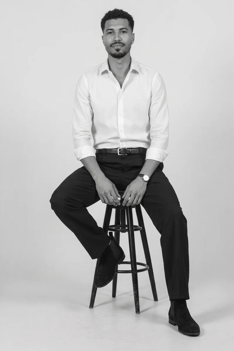 Miguel de los Santos sentado en un banco alto, de camisa blanca, pantalón negro y botas.